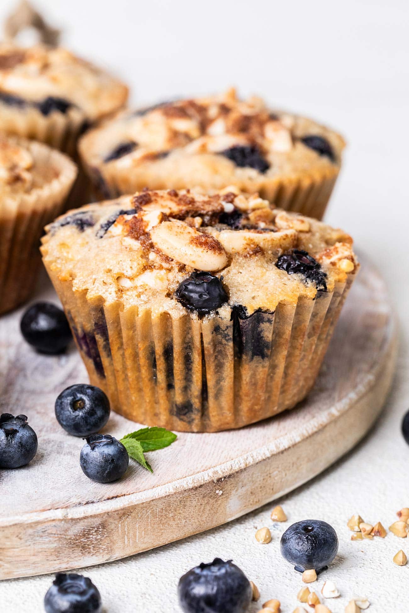 A buckwheat blueberry muffins sitting on a plate with blueberries and buckwheat groats.