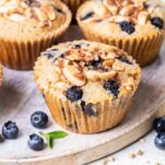A buckwheat muffin shown on a plate with blueberries scattered around it.