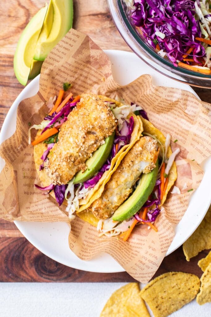 Fish tacos shown with a cabbage slaw and avocado slices.