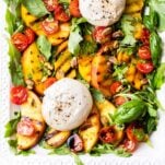 A close up look at a grilled peach salad topped with burrata cheese.
