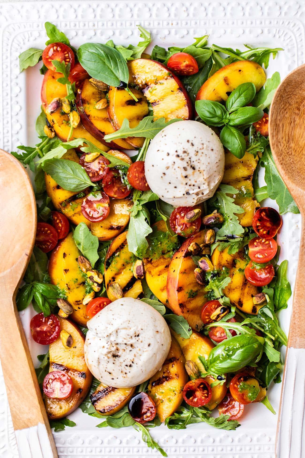 A grilled peach salad on a platter shown with large salad spoons.