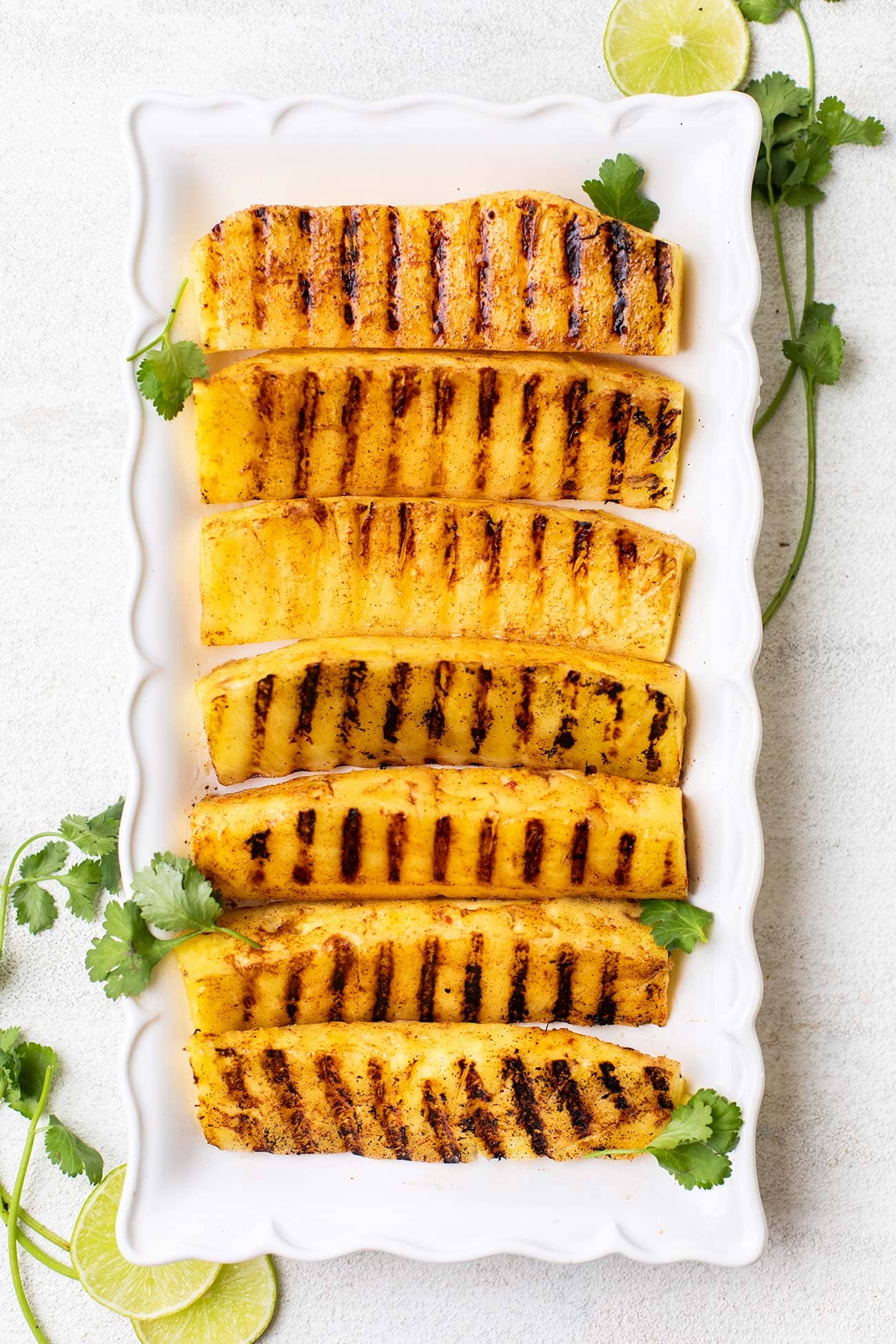 A platter of grilled pineapple garnished with cilantro and lime.