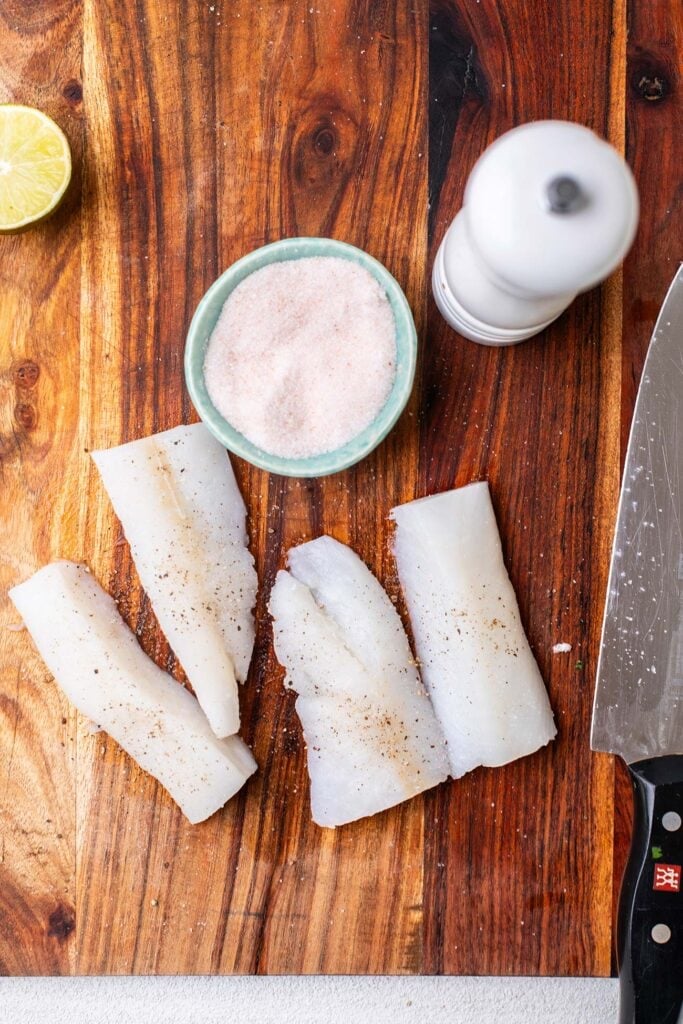 Chunks of cod being seasoned with salt and pepper.