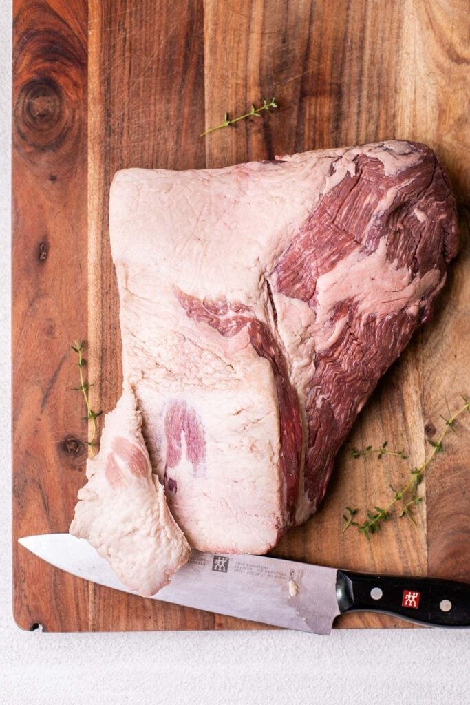 A whole beef brisket shown with the fat cap being trimmed.