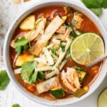 A bowl of chicken enchilada soup shown close up garnished with lime and cilantro.