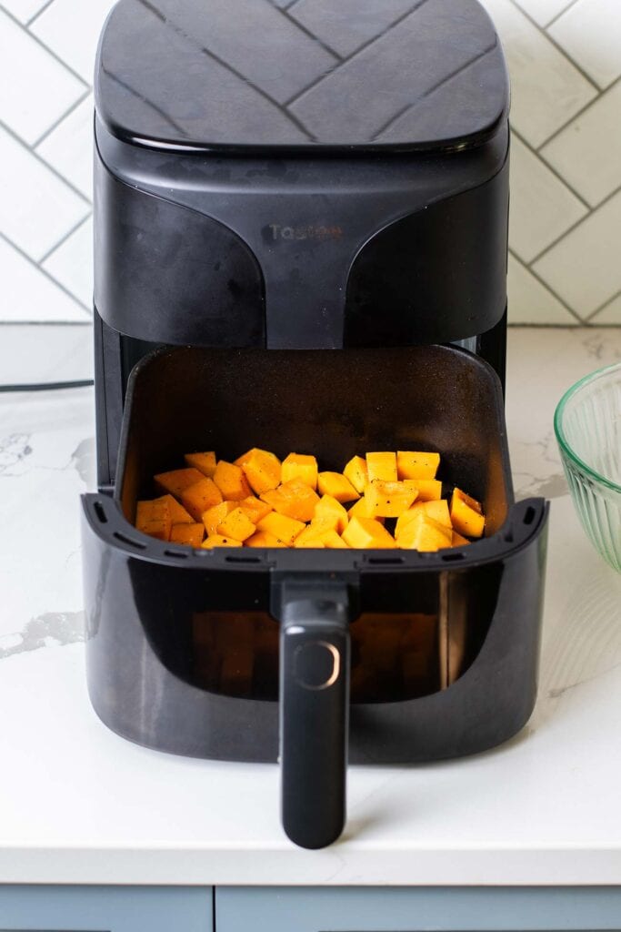 Butternut squash in an even layer in the air fryer basket.