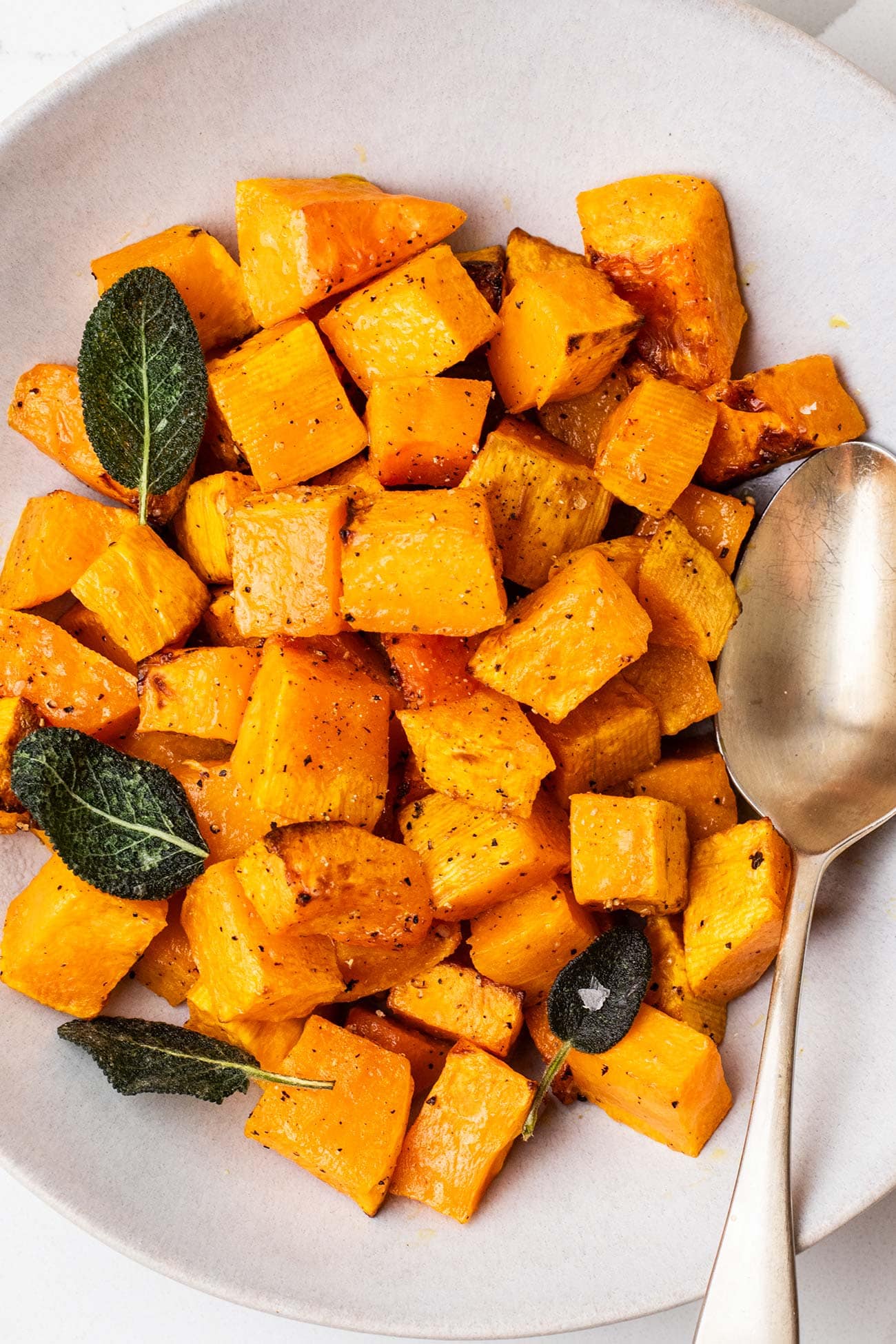 A bowl of air fryer butternut squash shown garnished with fried sage.