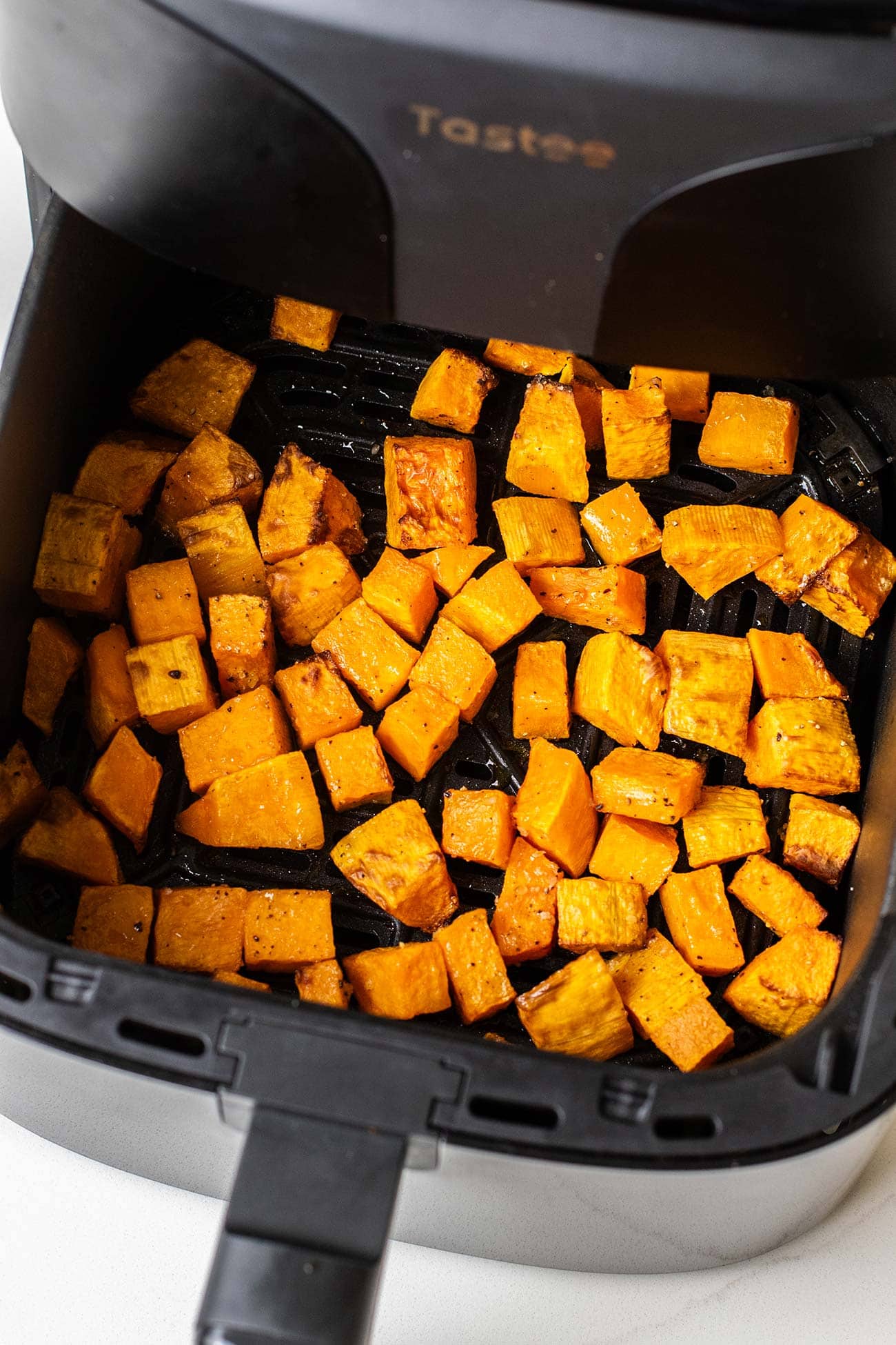 Butternut squash shown browned in an air fryer basket.