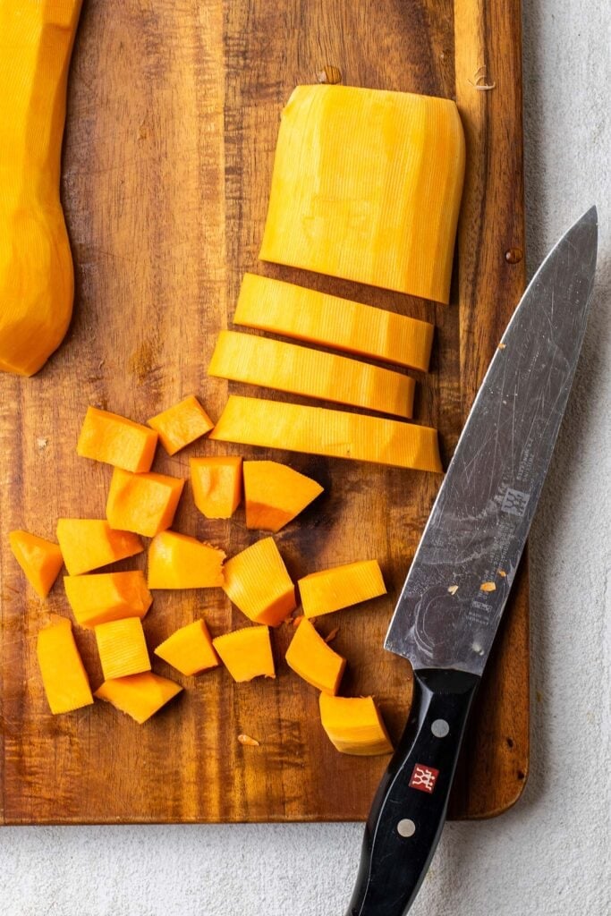 A squash cut in strips, then being cut into even sized cubes.