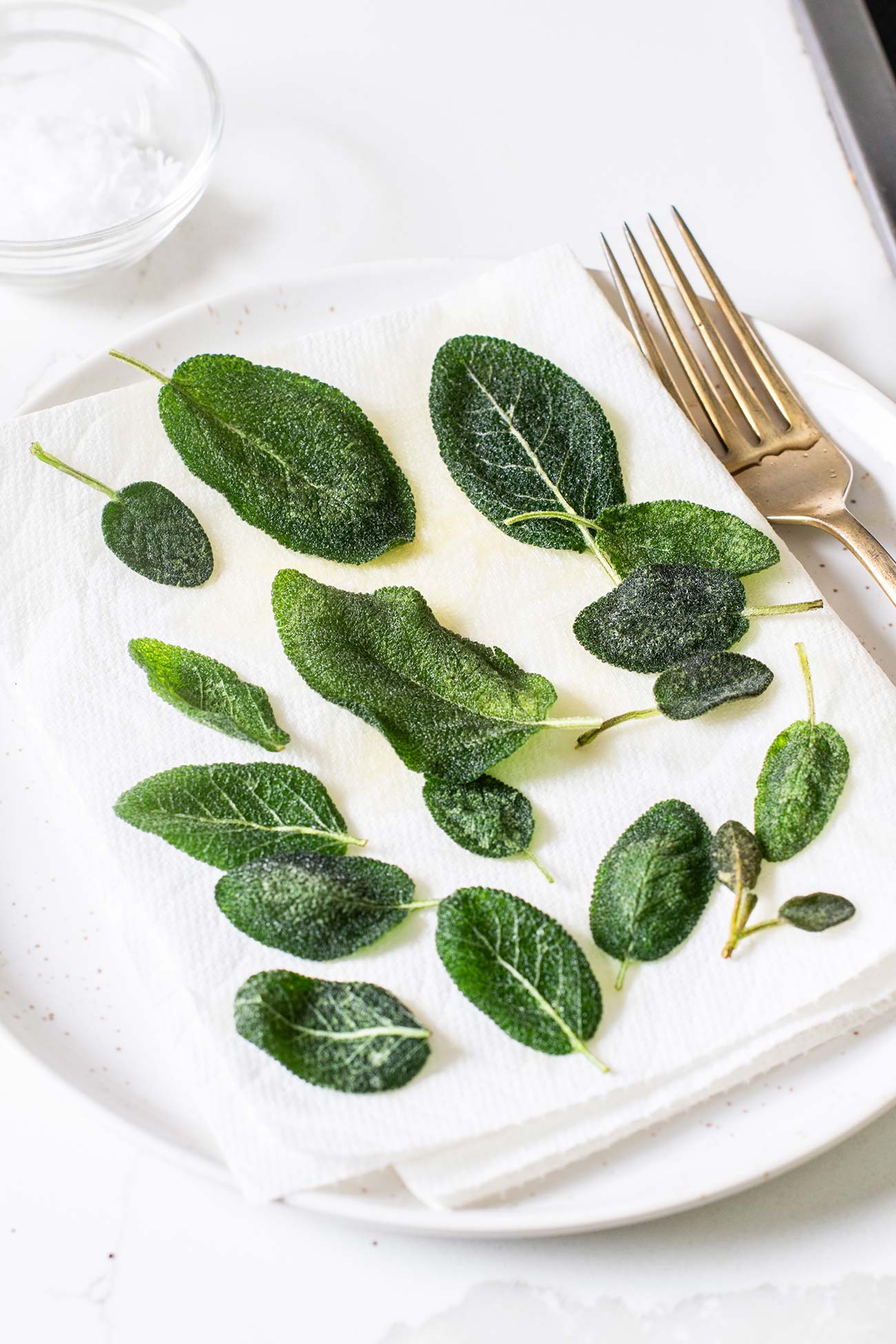 Darker green sage leaves sitting on a paper towel lined plate.