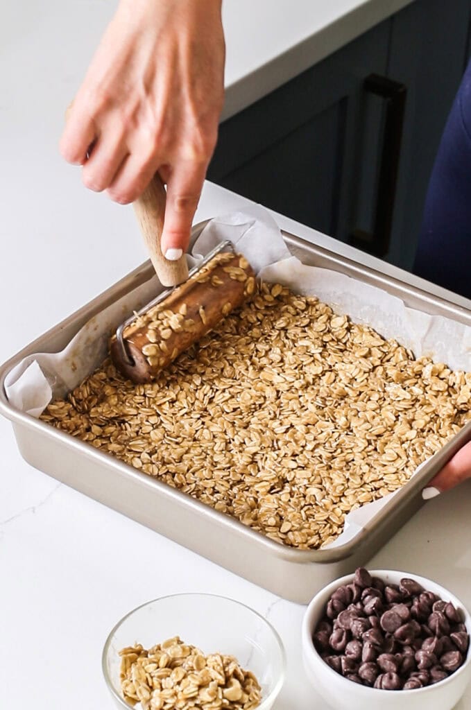 A layer of no bake oatmeal cookie batter being pressed into the bottom of the baking pan.