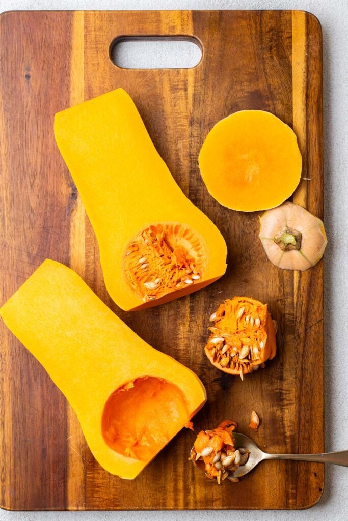 A peeled butternut squash cut in half with a spoon removing the pith and seeds.
