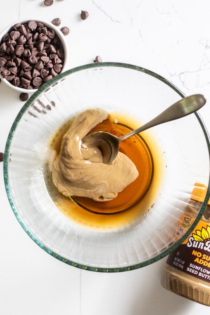 A large bowl shown with sunbutter, maple syrup, and coconut oil being mixed together.