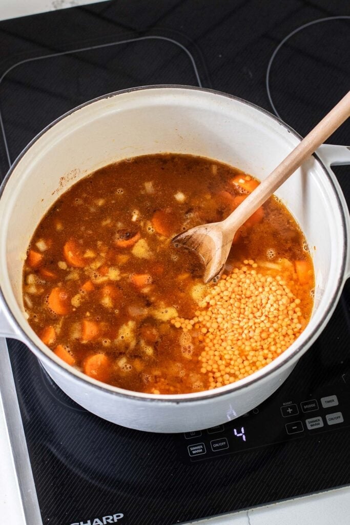 A dutch oven with vegetable broth, lentils ,and spices added to the carrots and onions.