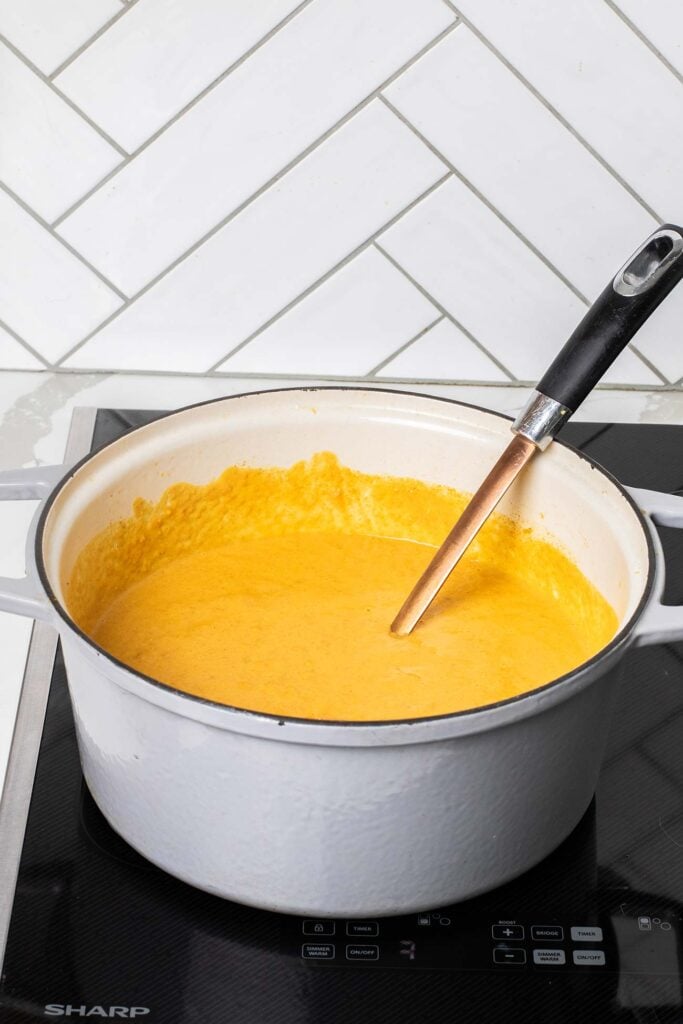 A pot of a vibrant orange soup shown with a ladle.