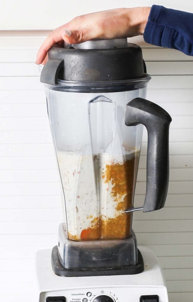 A blender shown filled with a carrot and lentil soup plus creamy coconut milk.