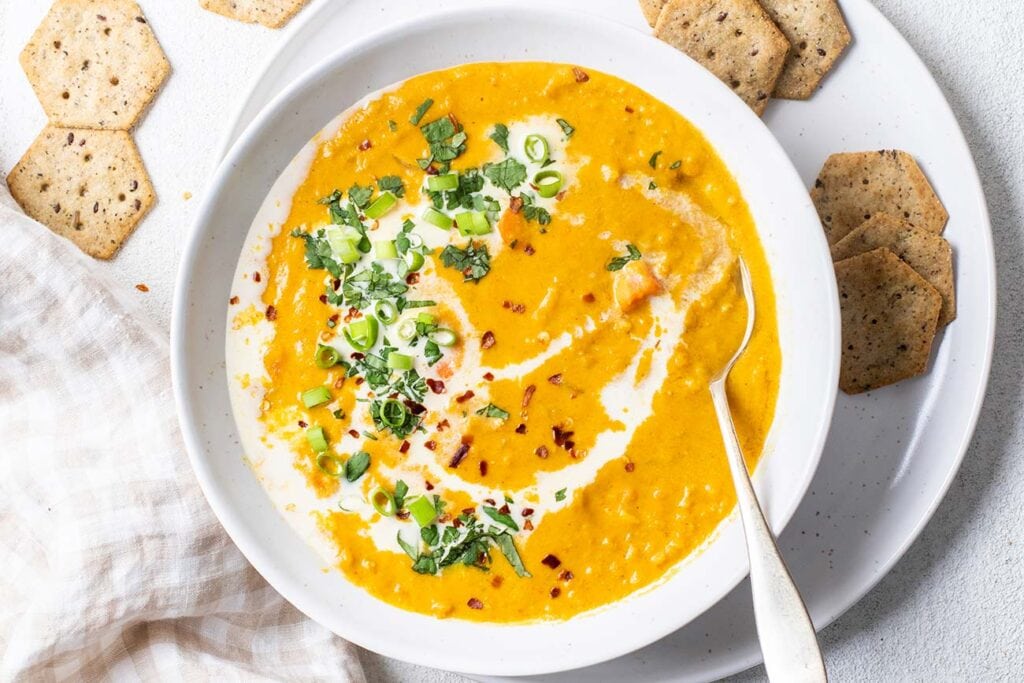A bowl of carrot and red lentil soup shown garnished with cilantro and green onions.