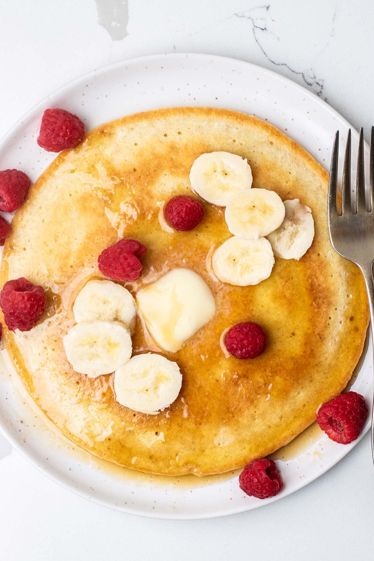 A cottage cheese pancake topped with raspberries and bananas.