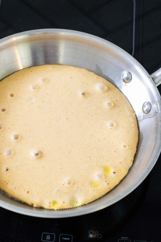 A pancake in a skillet showing bubbles forming around the edges.
