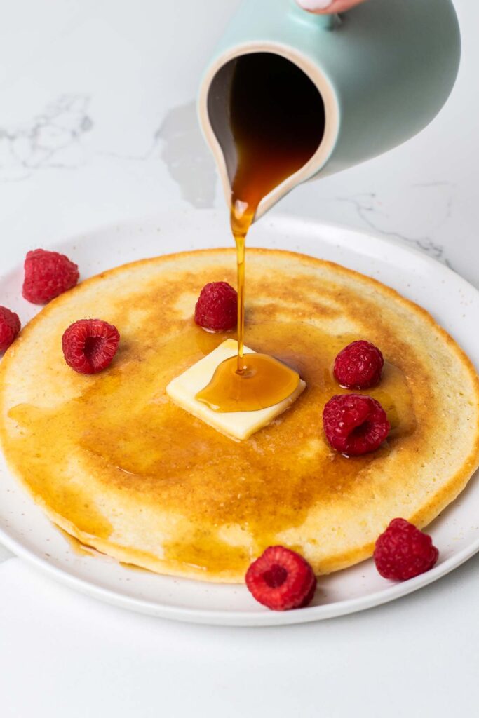 A pancake topped with berries being drizzled with maple syrup.