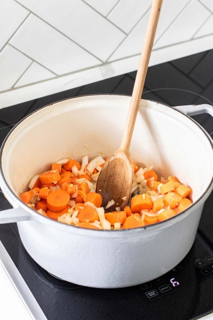 A dutch oven with carrots and onions being sauteed.