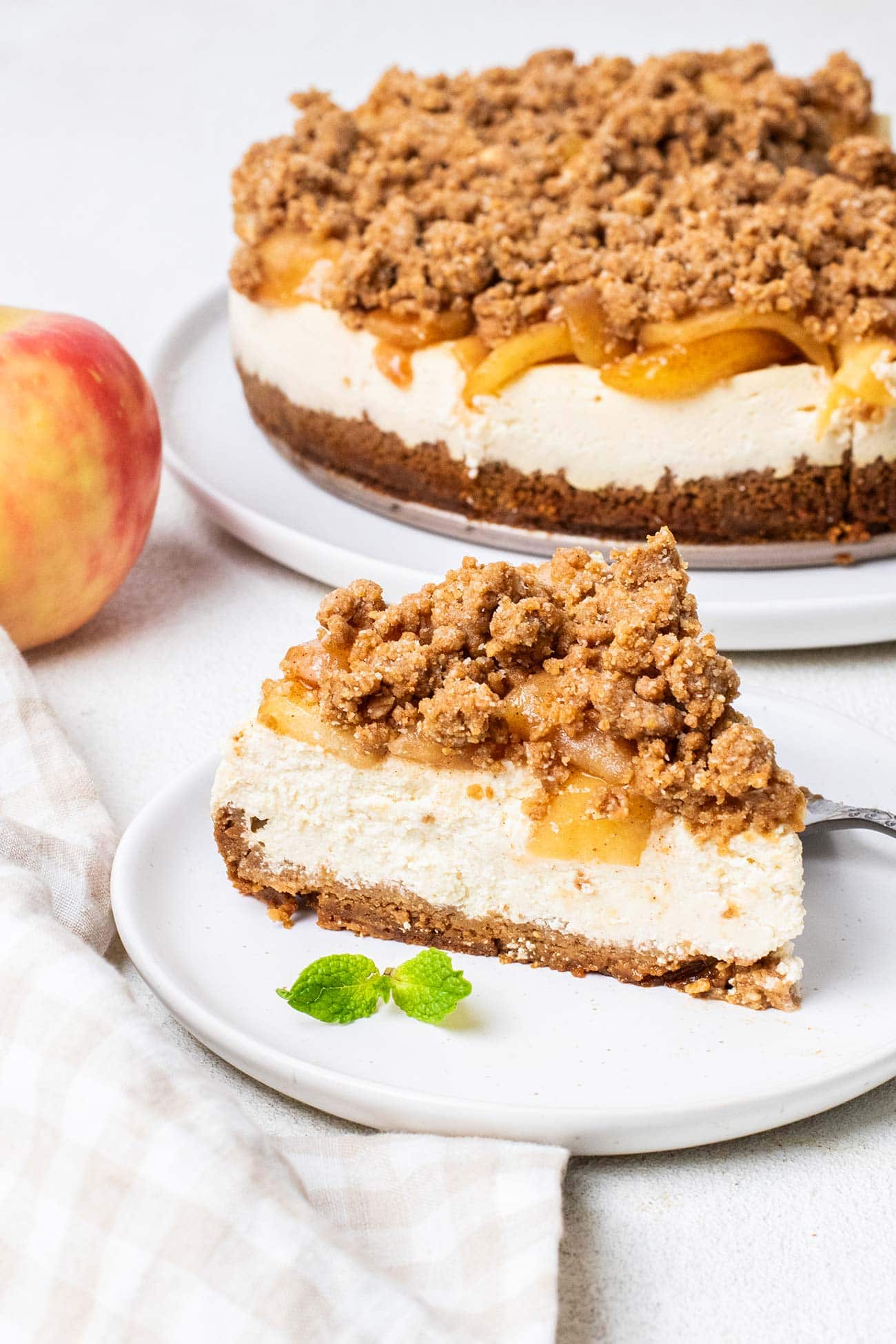 A slice of cheesecake on a plate in front of a whole apple pie cheesecake.