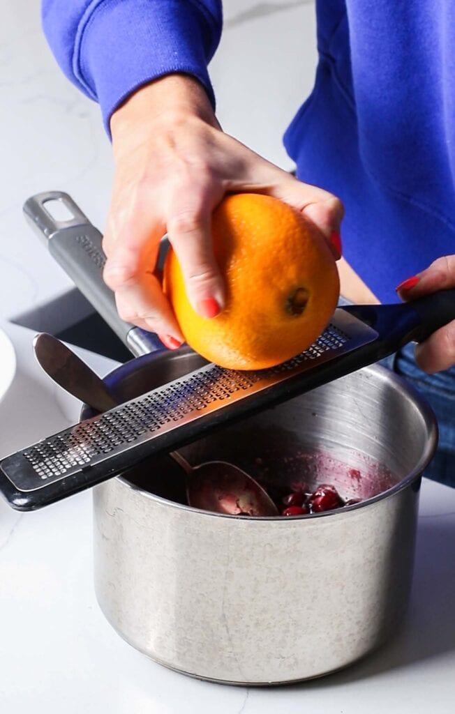Grating orange zest into a pan of cranberry sauce.
