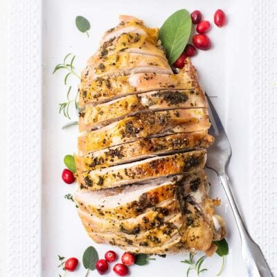 A turkey breast shown sliced and garnished with fresh cranberries and herbs.