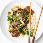 Beef with broccoli over cauliflower rice on a white plate.
