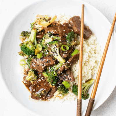 Beef with broccoli over cauliflower rice on a white plate.