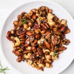A bowl of mixed nuts with a candy coating with shallots and rosemary.