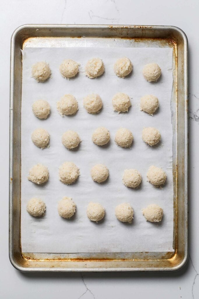 Balls of coconut macaroon dough on a baking sheet.