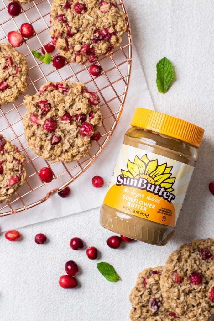 A jar of sunbutter sitting next to a cooling rack wtih cranberry oatmeal cookies.