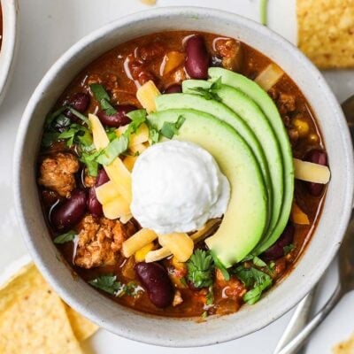 A close up look at a bowl of turkey chili, shown topped with sour cream and avocado slices.