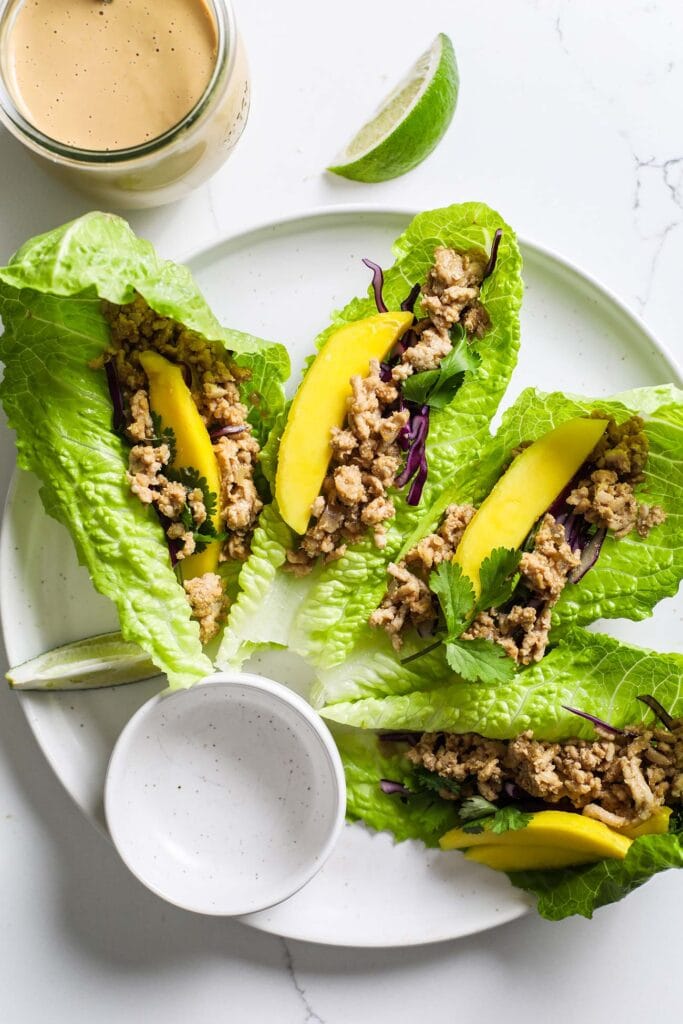 A white plate with lettuce leaves filled with mango, cabbage, and ground chicken.