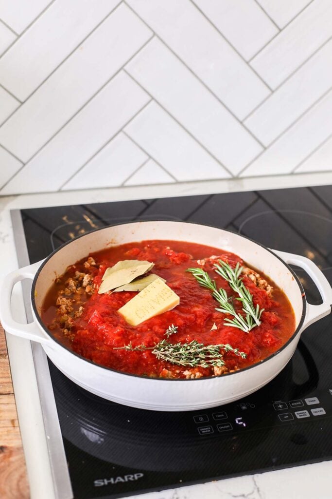 The pan showing adding chicken broth, crushed tomatoes, and herbs.