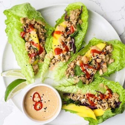 A plate with spicy Thai chicken lettuce wraps served with peanut sauce.