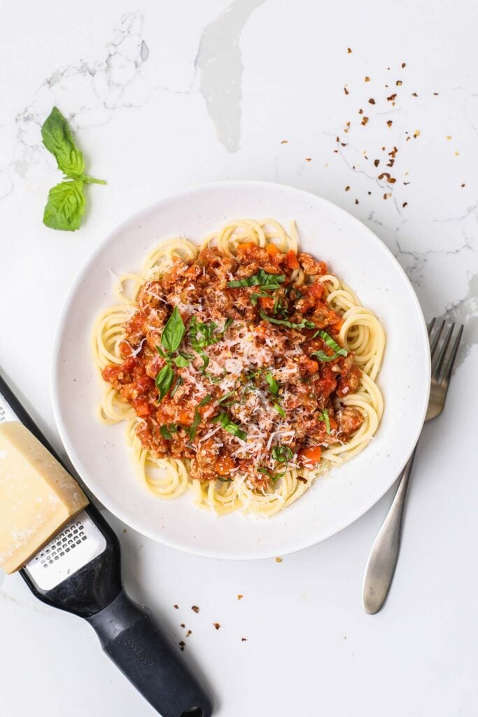 Turkey bolognese recipe shown served over pasta with parmesan cheese and basil.