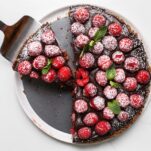 A whole raspberry chocolate tart shown with a slice being served.