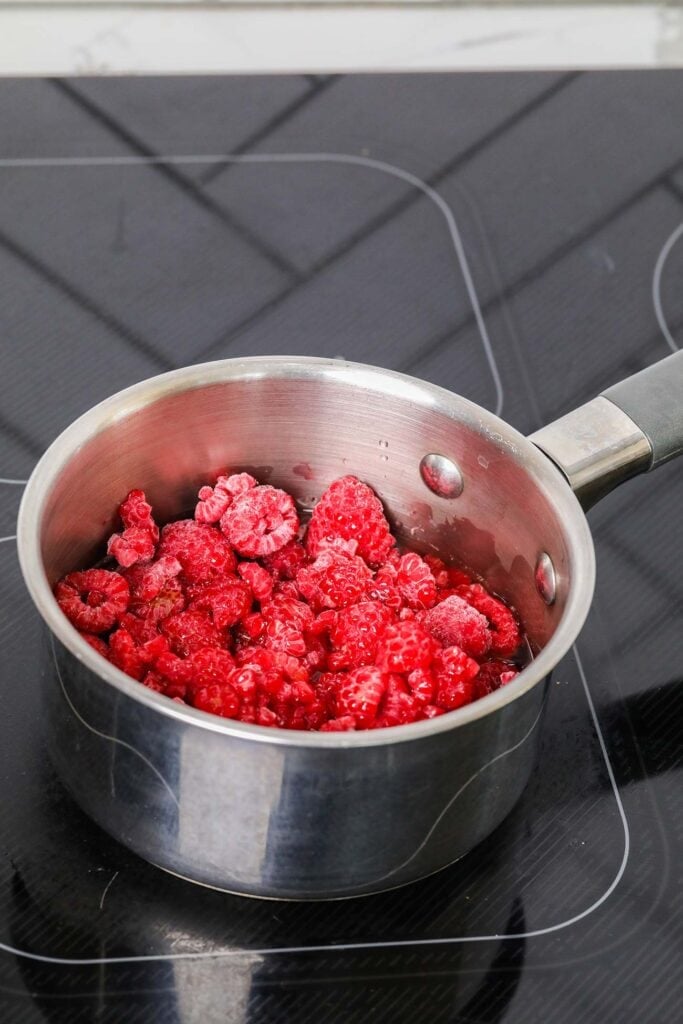 Raspberries simmering in a small saucepan.