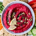 A vibrant pink beet hummus in a bowl on a platter of veggies.