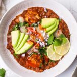 A bowl of slow cooker mexican chicken and rice, shown topped with avocado, onions, and cilantro.
