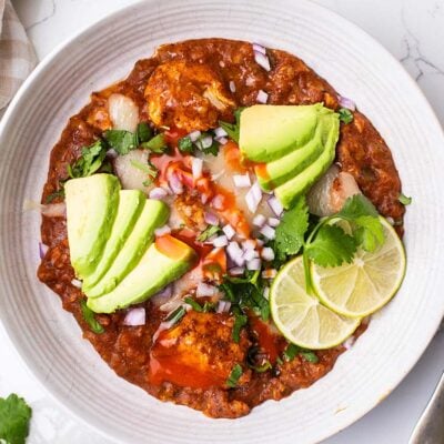 A bowl of slow cooker mexican chicken and rice, shown topped with avocado, onions, and cilantro.