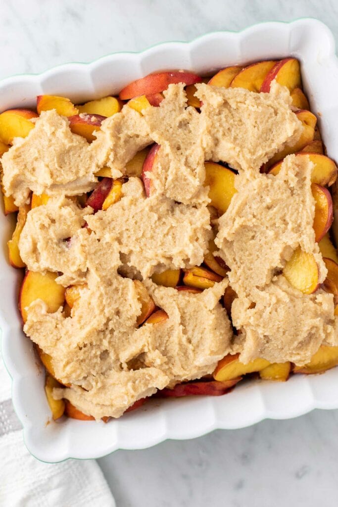 Thick cobbler dough spread over the top of peaches.