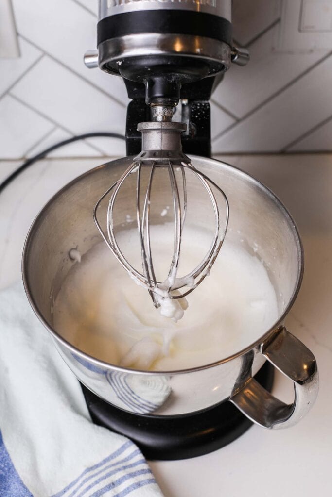 Eggs whites being whipped into stiff peaks in a stand mixer.