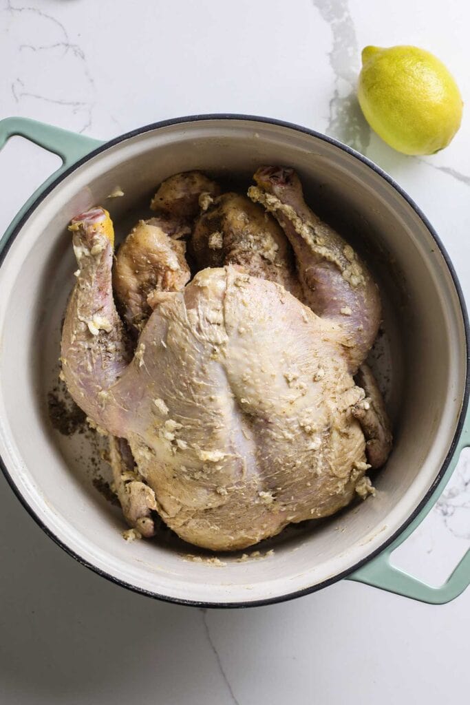 A whole chicken in a dutch oven coated in lemon butter.