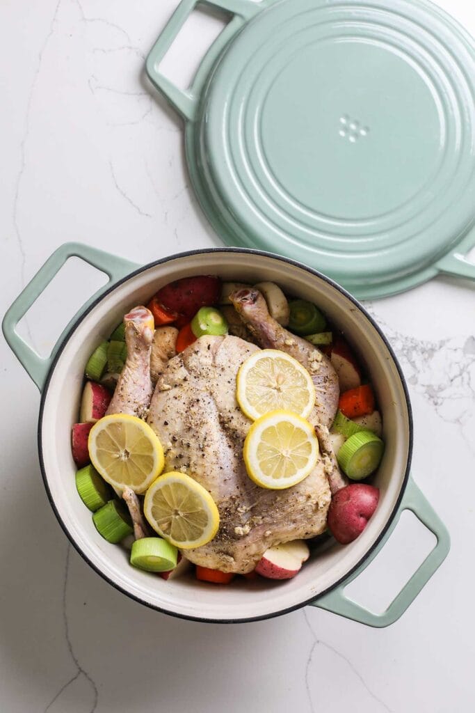 A chicken in a dutch oven surrounded by colorful veggies.