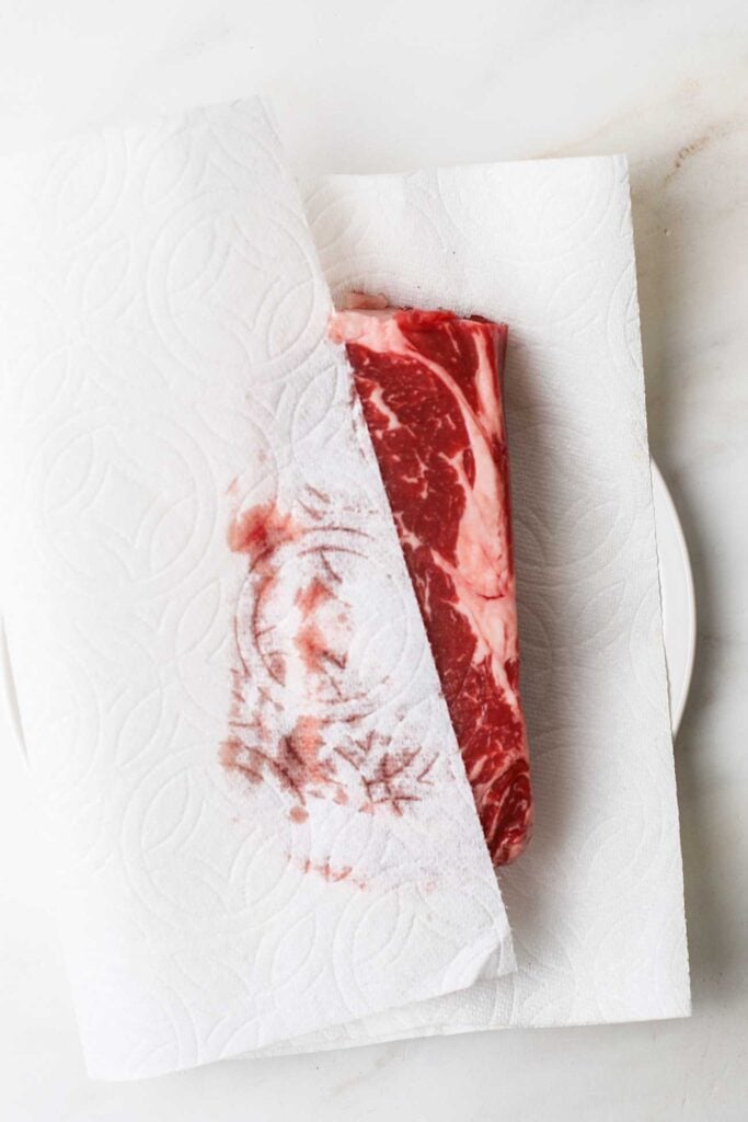 A steak being dried with a paper towel prior to seasoning.