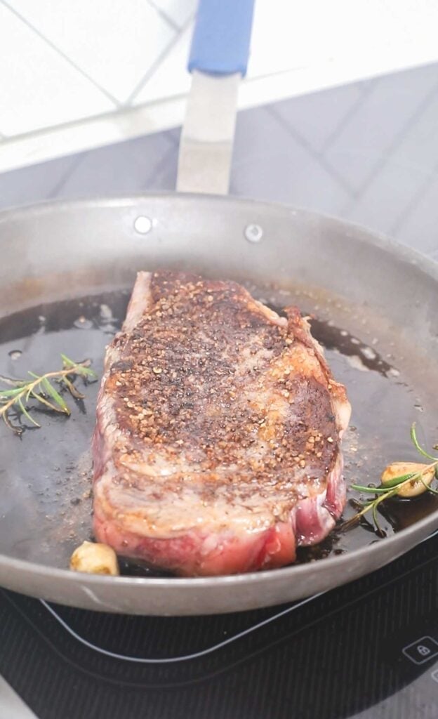 A steak flipped over in the pan to reveal a deep crust.