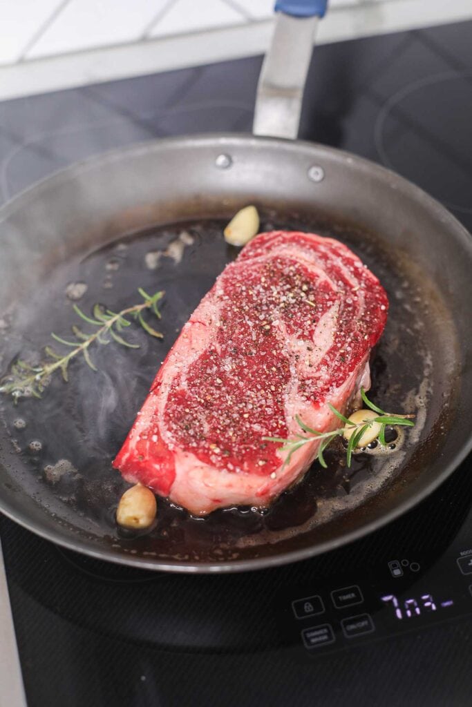 A steak added to a pan with hot oil and butter.